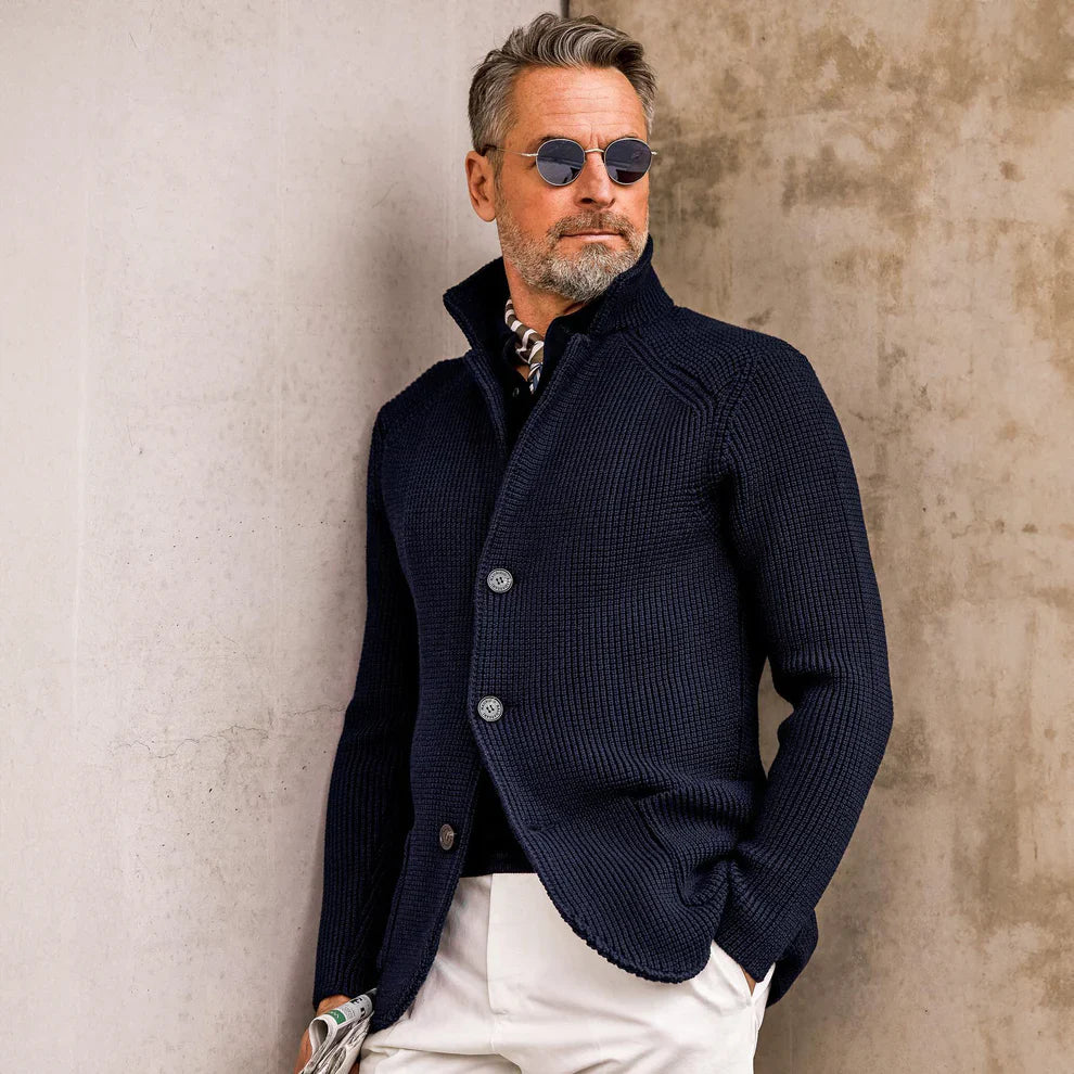 Man wearing a navy blue knitted cardigan against a textured wall