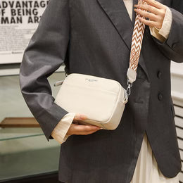 Person holding a beige handbag with a patterned strap in an indoor setting