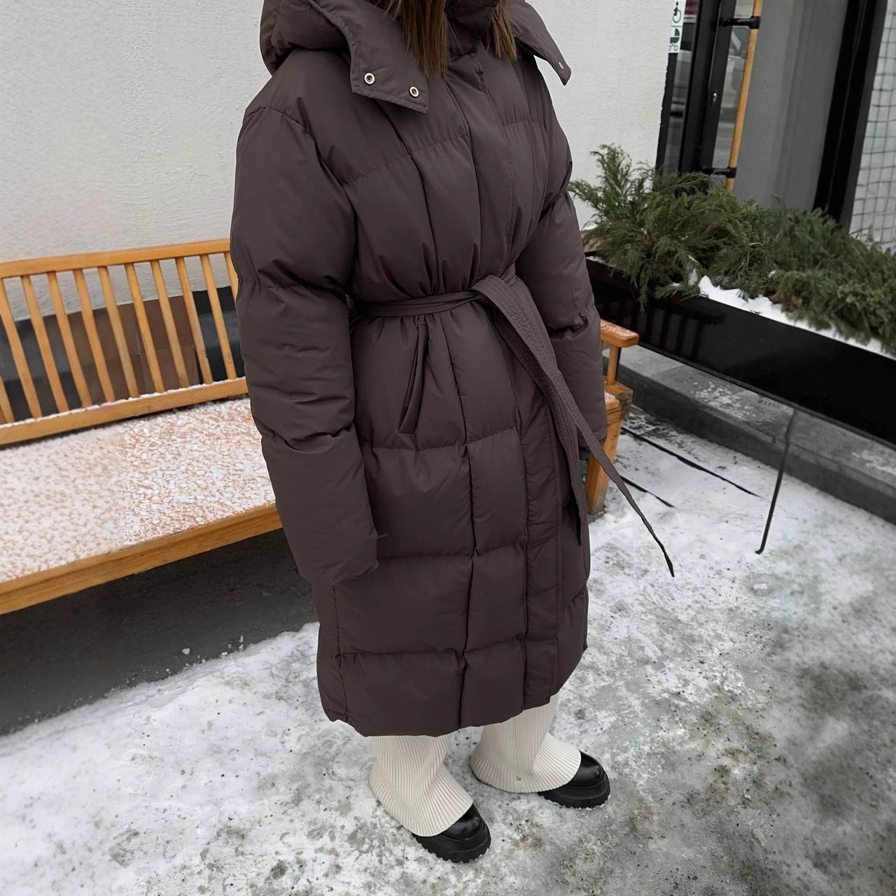 Person wearing a long brown puffer coat standing on a snowy ground.