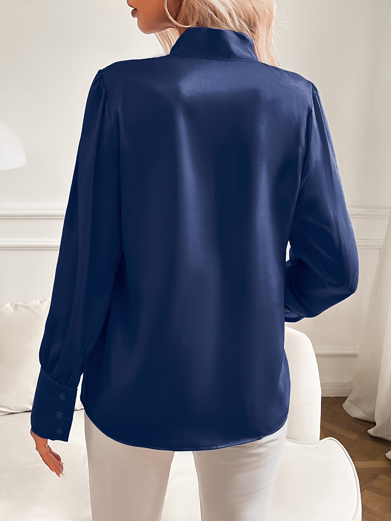 Person wearing a navy blue satin shirt in a room with white walls and furniture.