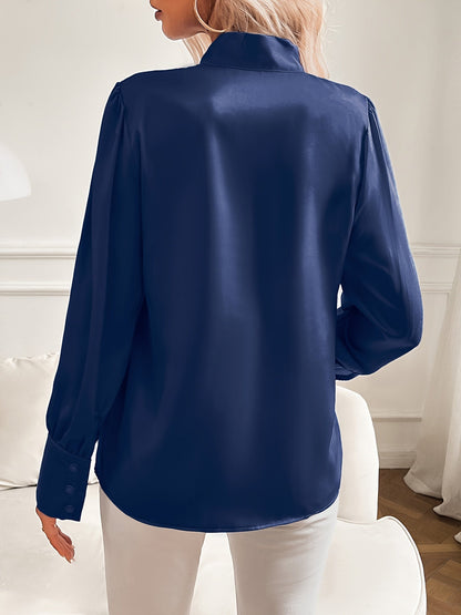 Person wearing a navy blue satin shirt in a room with white walls and furniture.