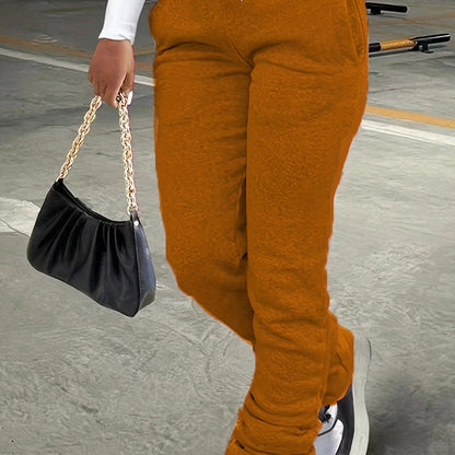 Person wearing orange pants and holding a black handbag with a gold chain strap on a concrete surface.