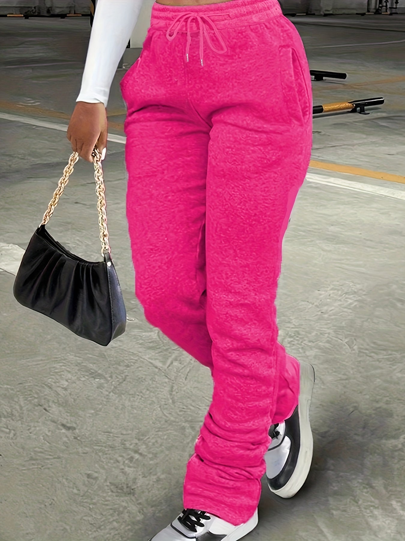 Person wearing bright pink sweatpants holding a black handbag on a concrete surface.