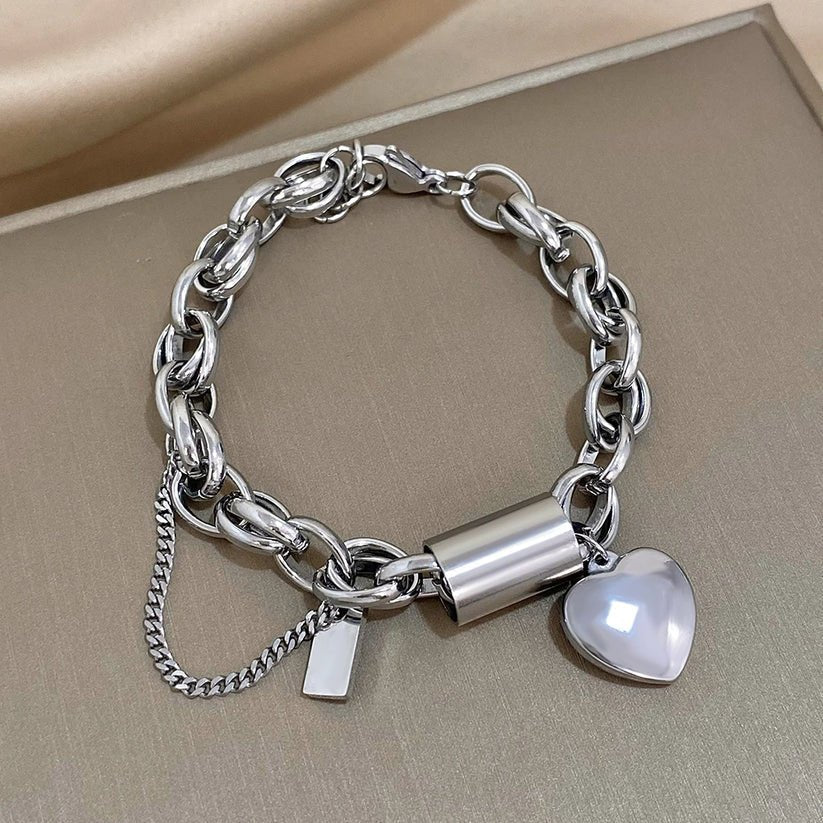 Silver chain bracelet with a heart-shaped charm on a beige surface