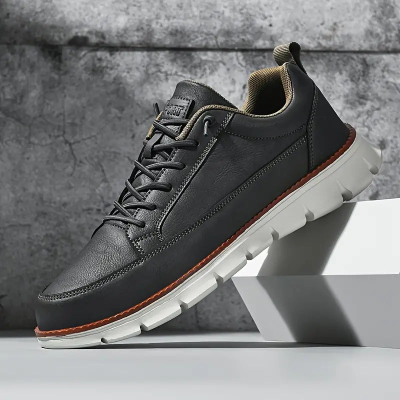 Black leather shoe with white sole on a gray background