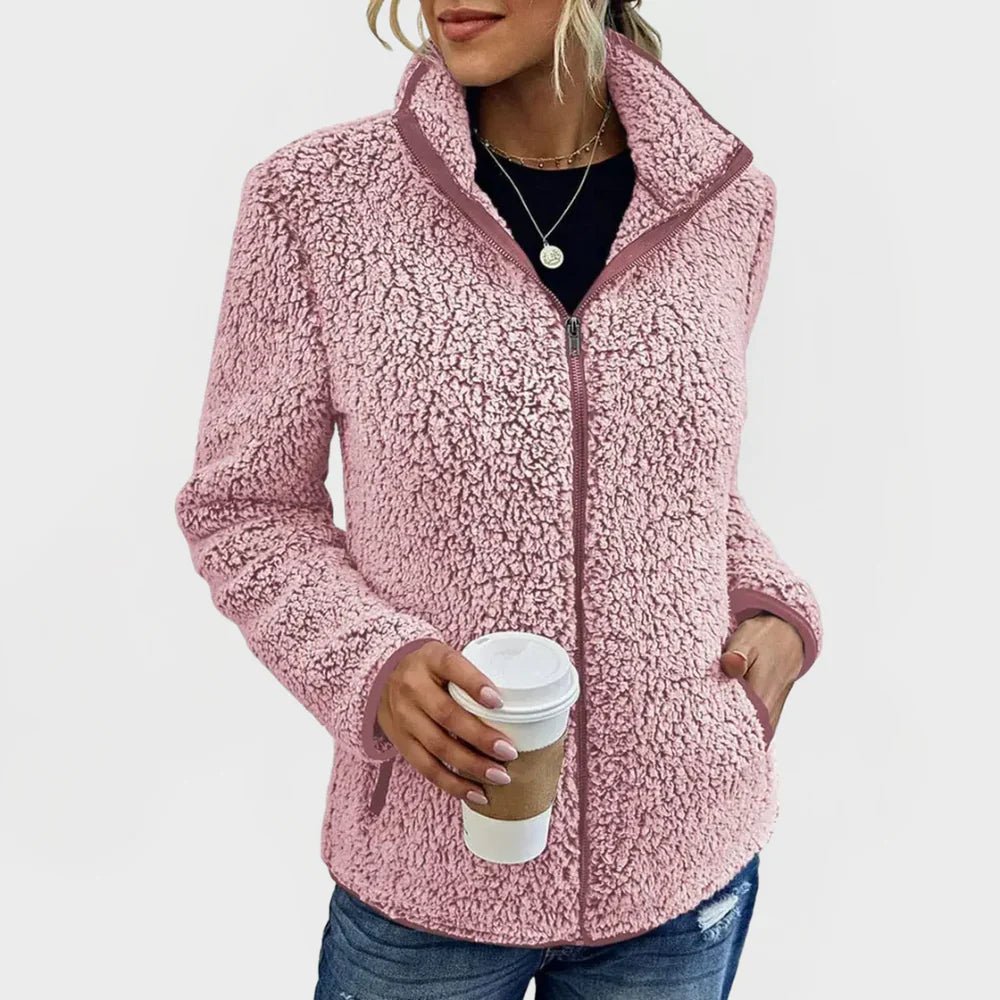 Person wearing a pink sherpa jacket holding a coffee cup on a white background
