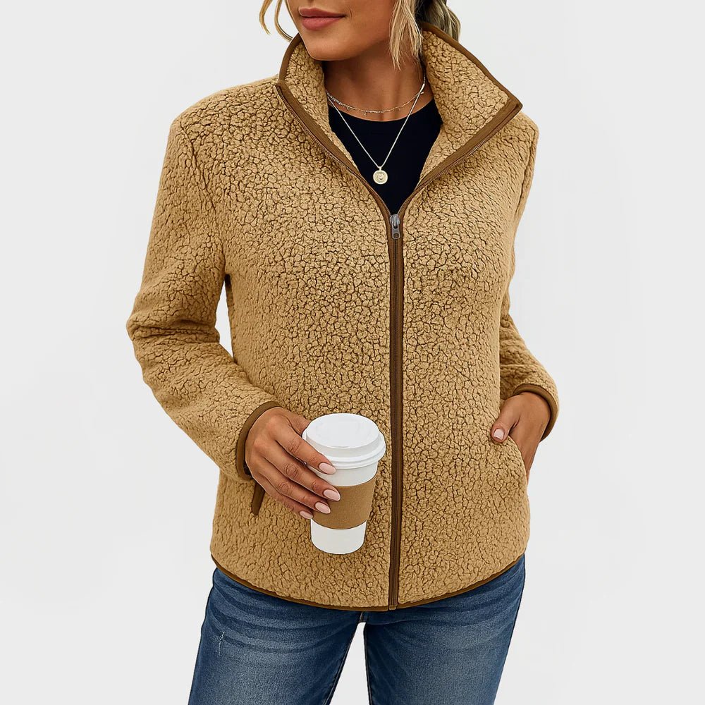 Person wearing a beige fleece jacket holding a coffee cup on a plain background