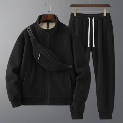 Black tracksuit with jacket and pants on hangers against a gray background