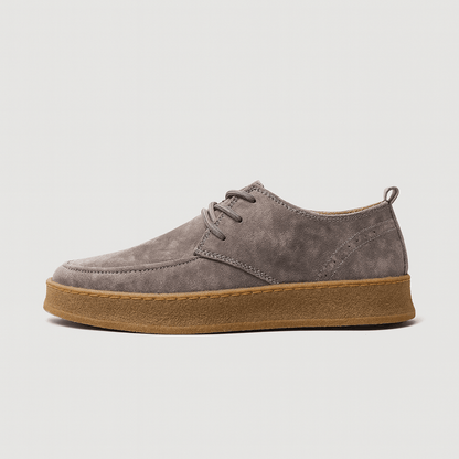 Gray suede shoe with brown sole on a light gray background