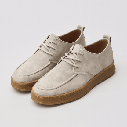 Pair of beige suede shoes with brown soles on a light gray background