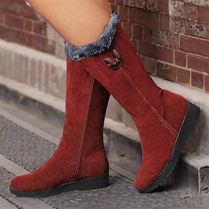 Red suede boots with black soles worn by a person on a brick sidewalk.