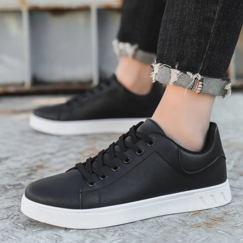Black sneakers with white soles worn by a person on a textured surface.