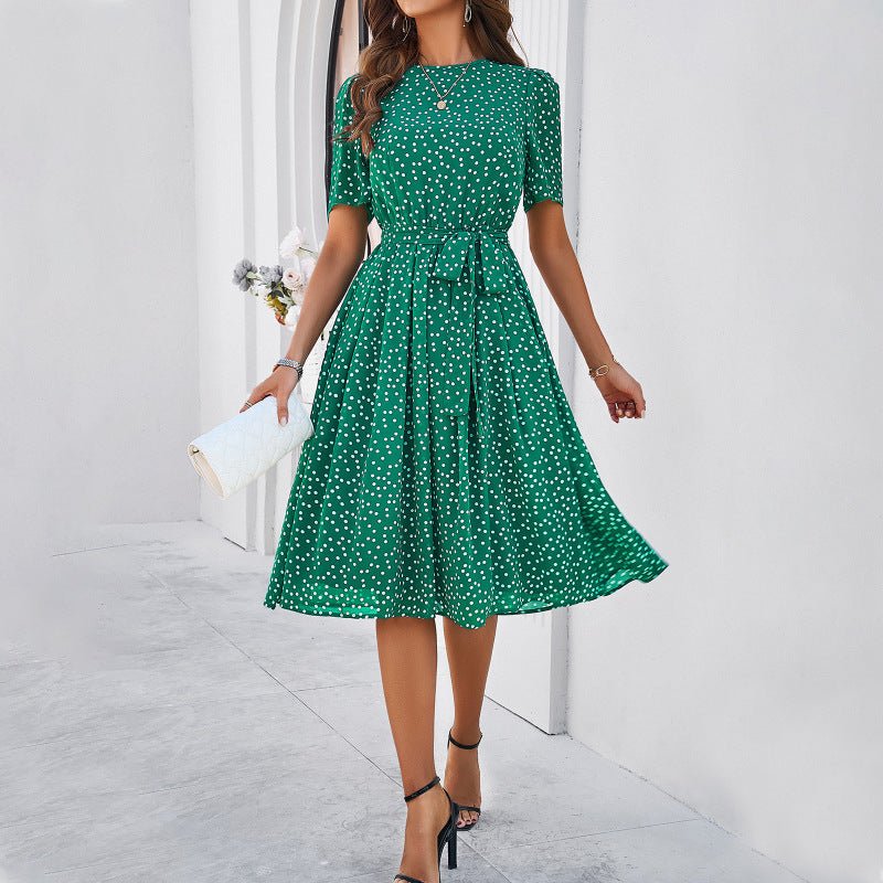 Woman wearing a green polka dot dress holding a white clutch against a light background