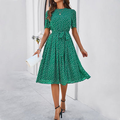 Woman wearing a green polka dot dress holding a white clutch against a light background