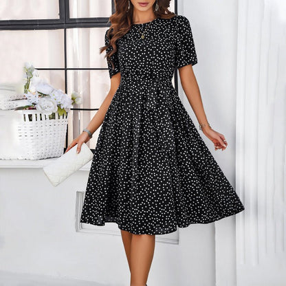Woman wearing a black dress with white polka dots in a bright room.