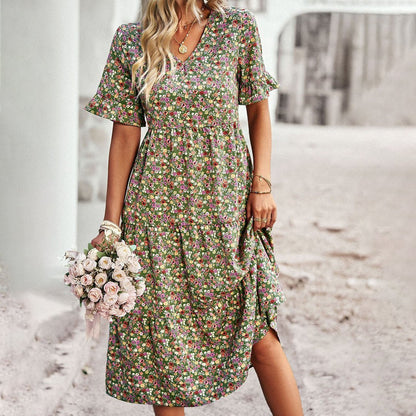 Woman wearing a floral dress holding flowers on a beach.