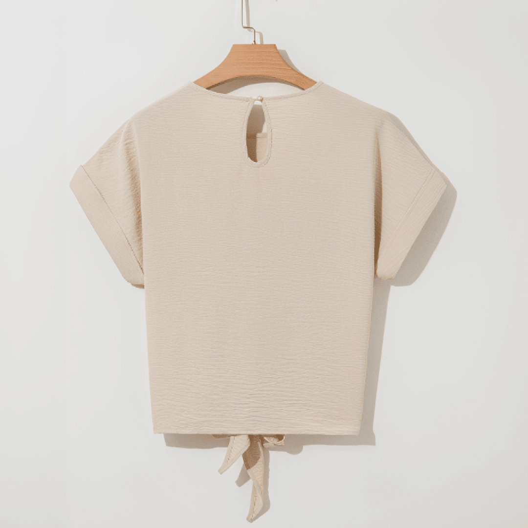 Beige top with a tie detail on a hanger against a white background