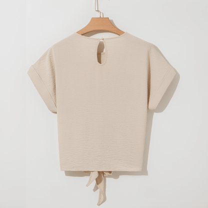 Beige top with a tie detail on a hanger against a white background