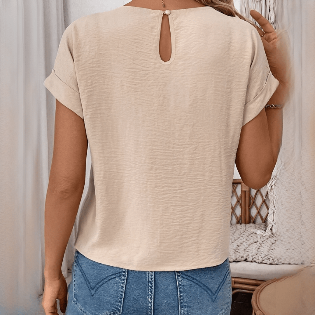 Person wearing a beige top with a cut-out back design, standing against a neutral background.