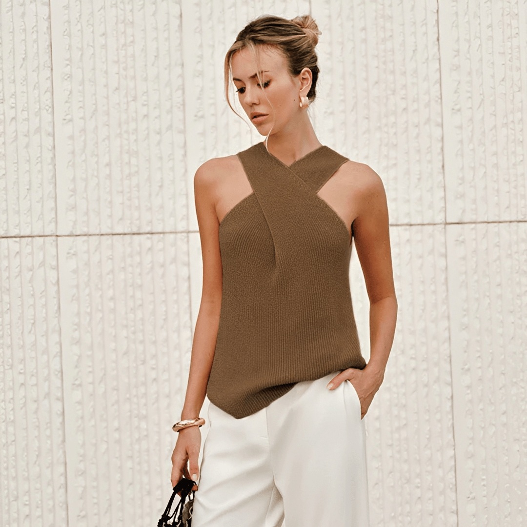 Woman wearing a brown sleeveless top and white pants against a textured wall.