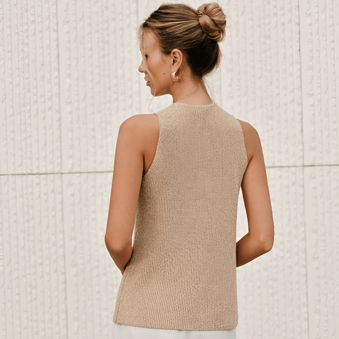 Woman wearing a beige knitted vest against a light tiled wall.