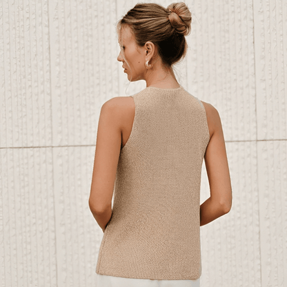 Woman wearing a beige knitted vest against a light tiled wall.