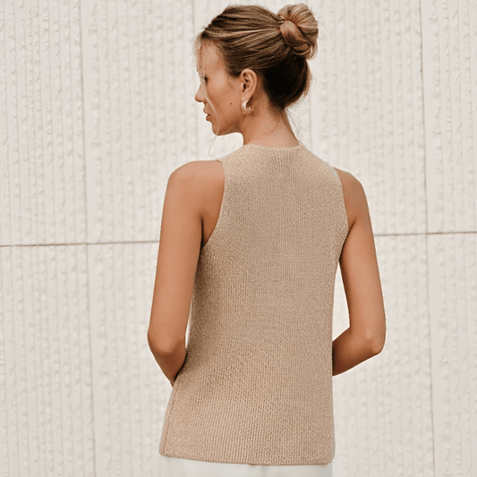 Woman wearing a beige knitted vest against a light tiled wall.