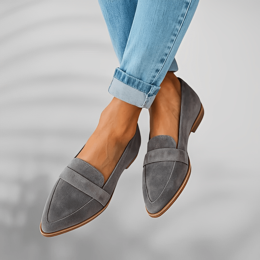 Gray loafers worn with rolled-up blue jeans on a neutral background