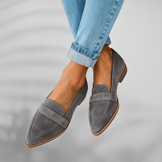 Gray loafers worn with rolled-up blue jeans on a neutral background
