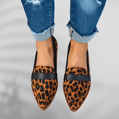 Leopard print loafers with black accents worn with rolled-up jeans on a gray background
