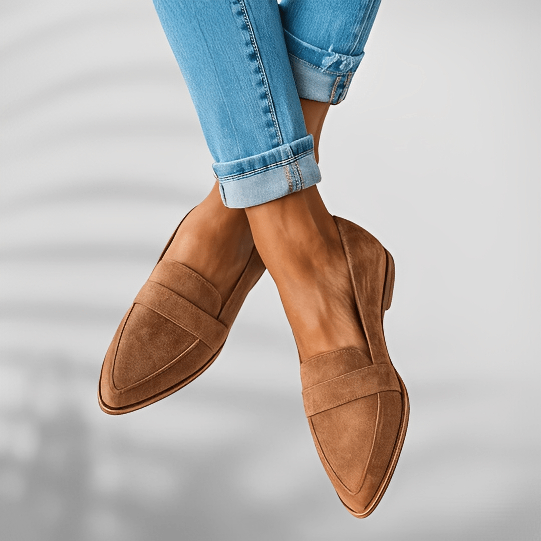 Brown loafers worn with rolled-up blue jeans on a light gray background