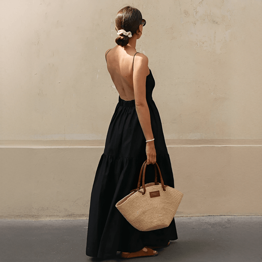 Woman in a black dress holding a straw bag against a beige wall