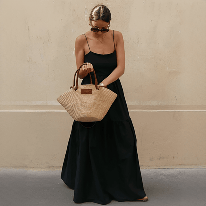 Woman holding a woven handbag against a plain wall