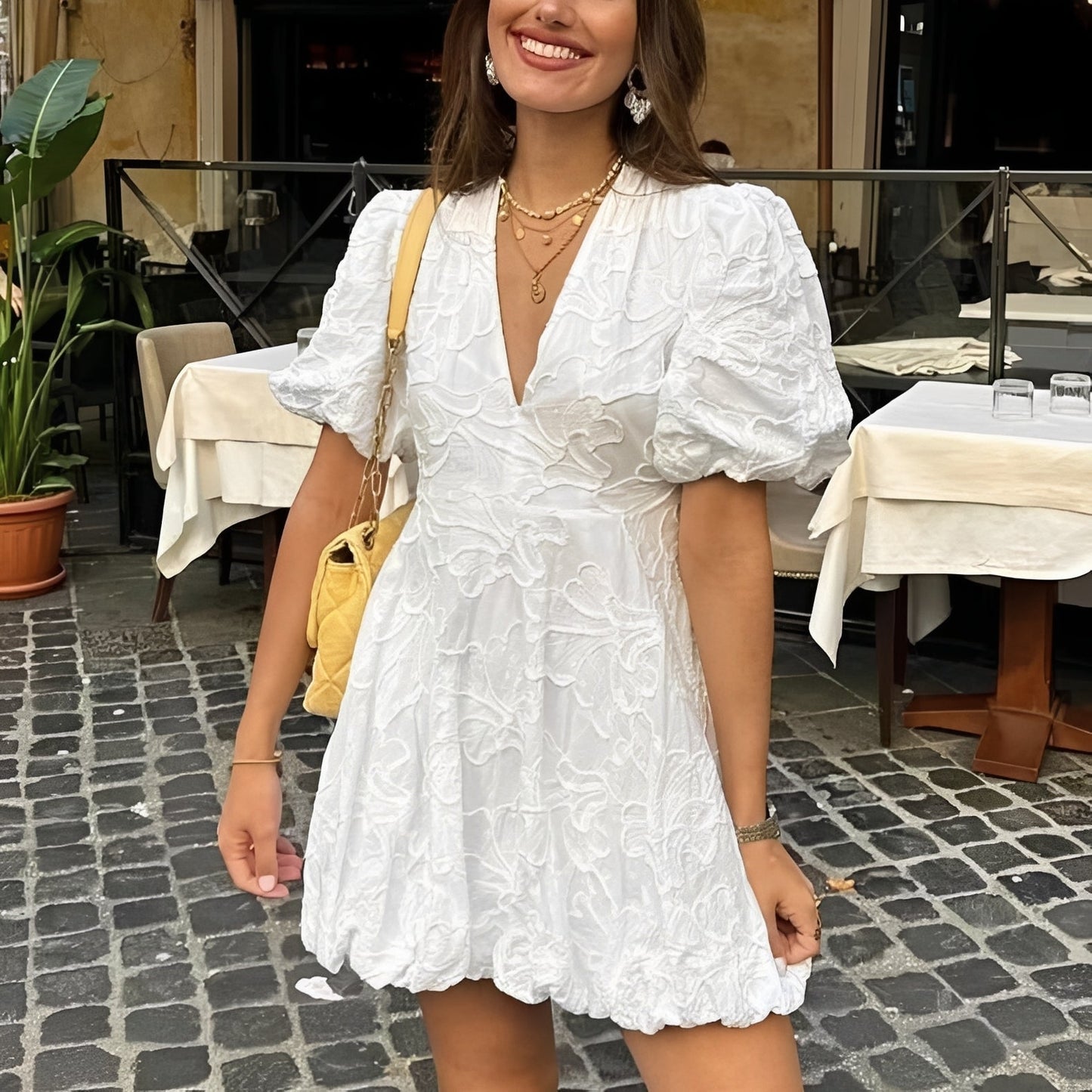 Woman in a white dress standing on a street with tables and chairs in the background