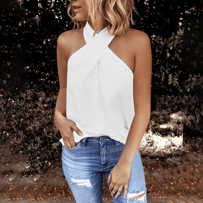 Woman wearing a white halter top and blue jeans standing outdoors.