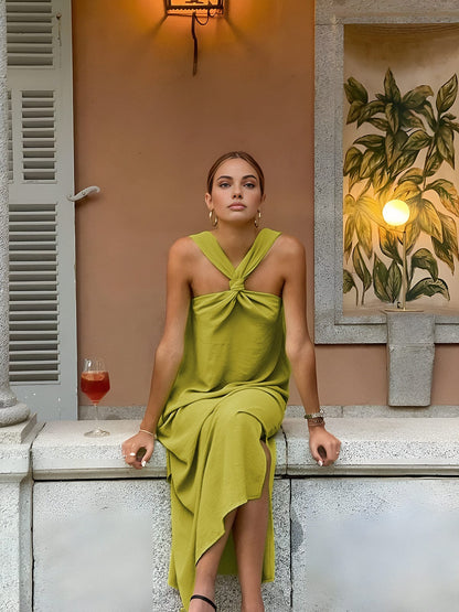 Woman in a green dress sitting on a ledge with a drink, surrounded by warm lighting and decor.