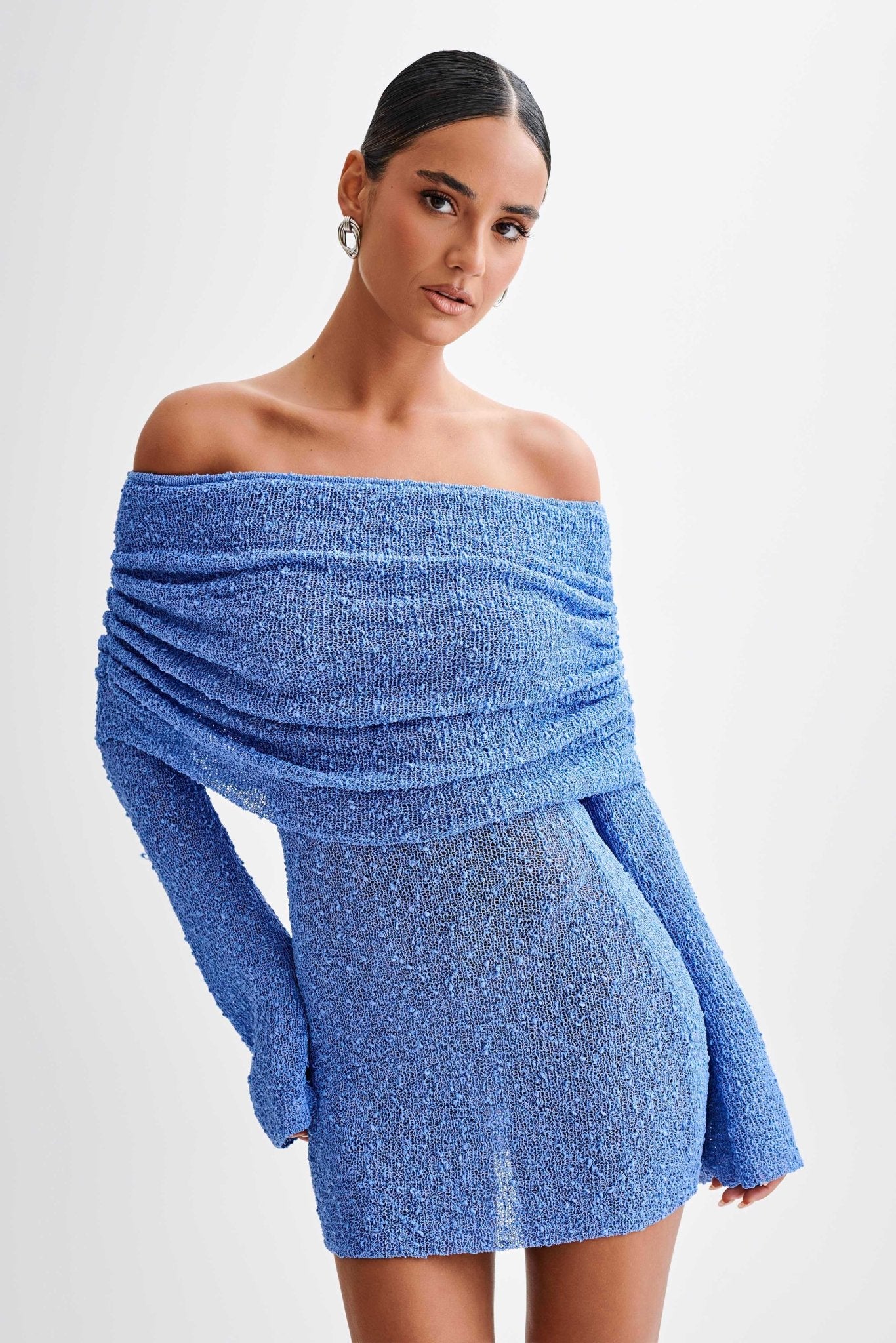 Woman wearing a blue off-shoulder dress against a white background