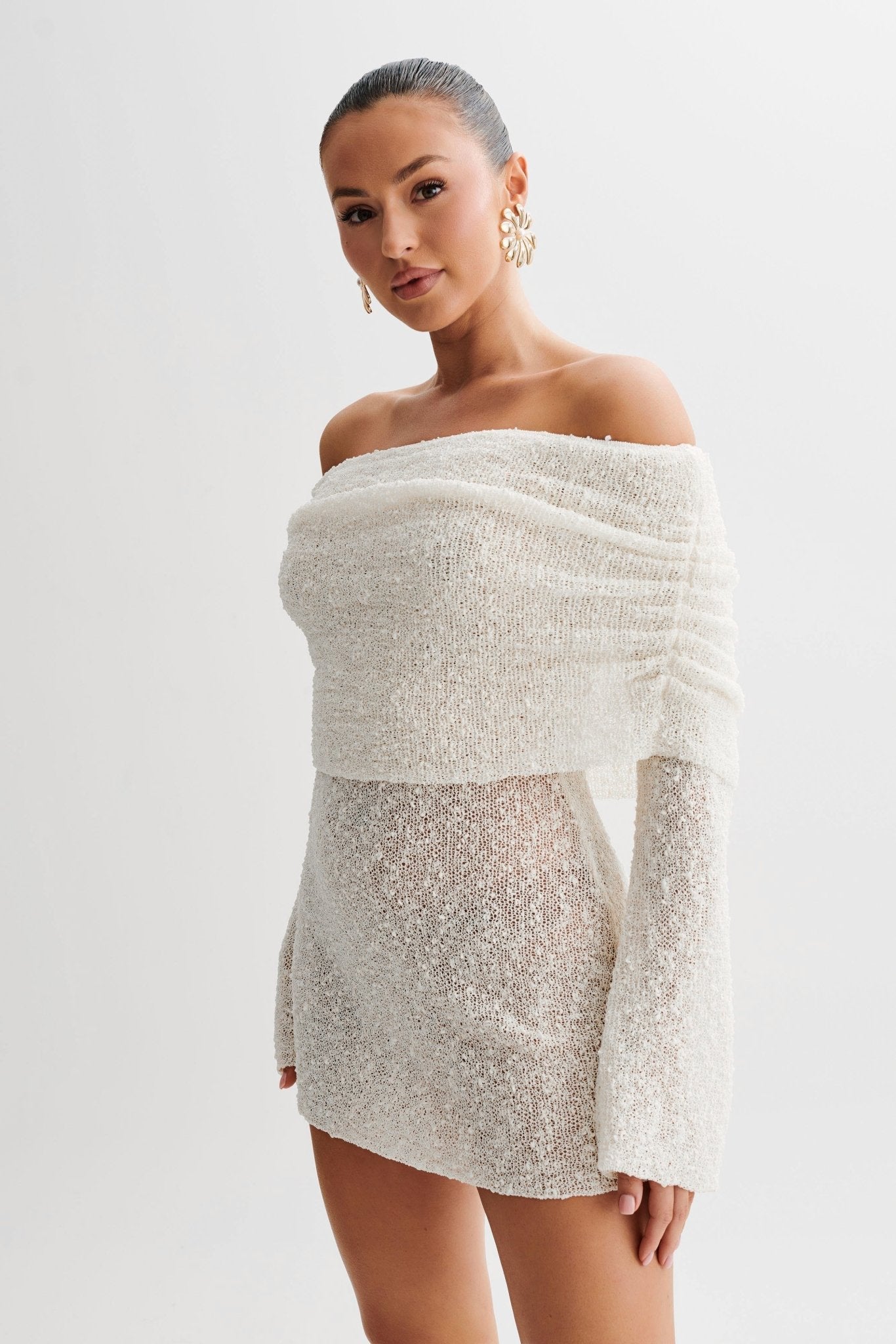 Woman wearing a white off-shoulder dress with sequin details on a plain background