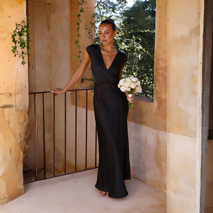 Woman in a black dress holding flowers on a balcony with stone walls and greenery.