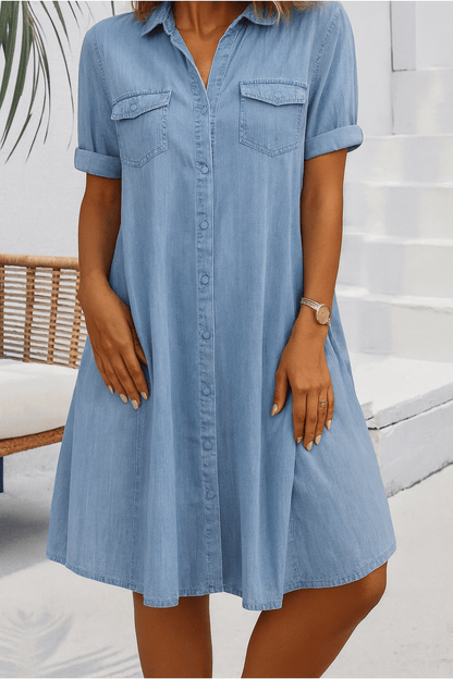 Woman wearing a light blue denim dress standing outdoors.