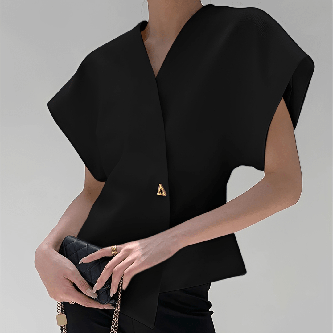 Black sleeveless top with a gold triangle detail held by a person against a gray background