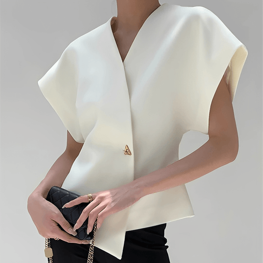 Person wearing a white sleeveless top with a brand logo, holding a black clutch against a neutral background