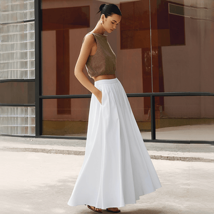 Woman in a brown top and white skirt standing in front of a modern building.