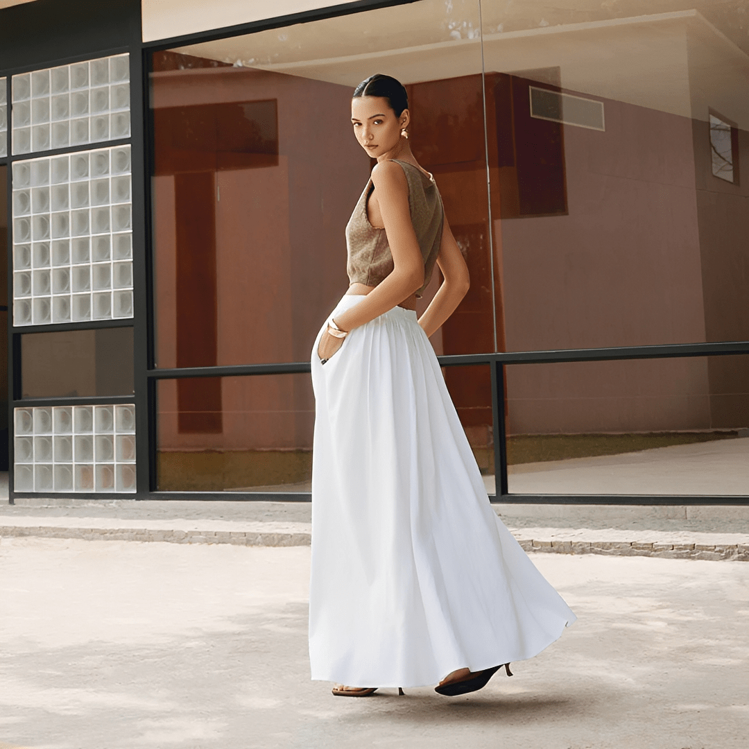 Woman in a beige top and white pants standing in front of a modern building.