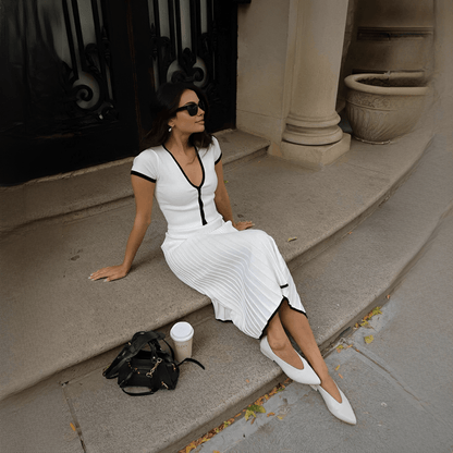 Woman in a white dress sitting on steps with a black handbag and coffee cup beside her.