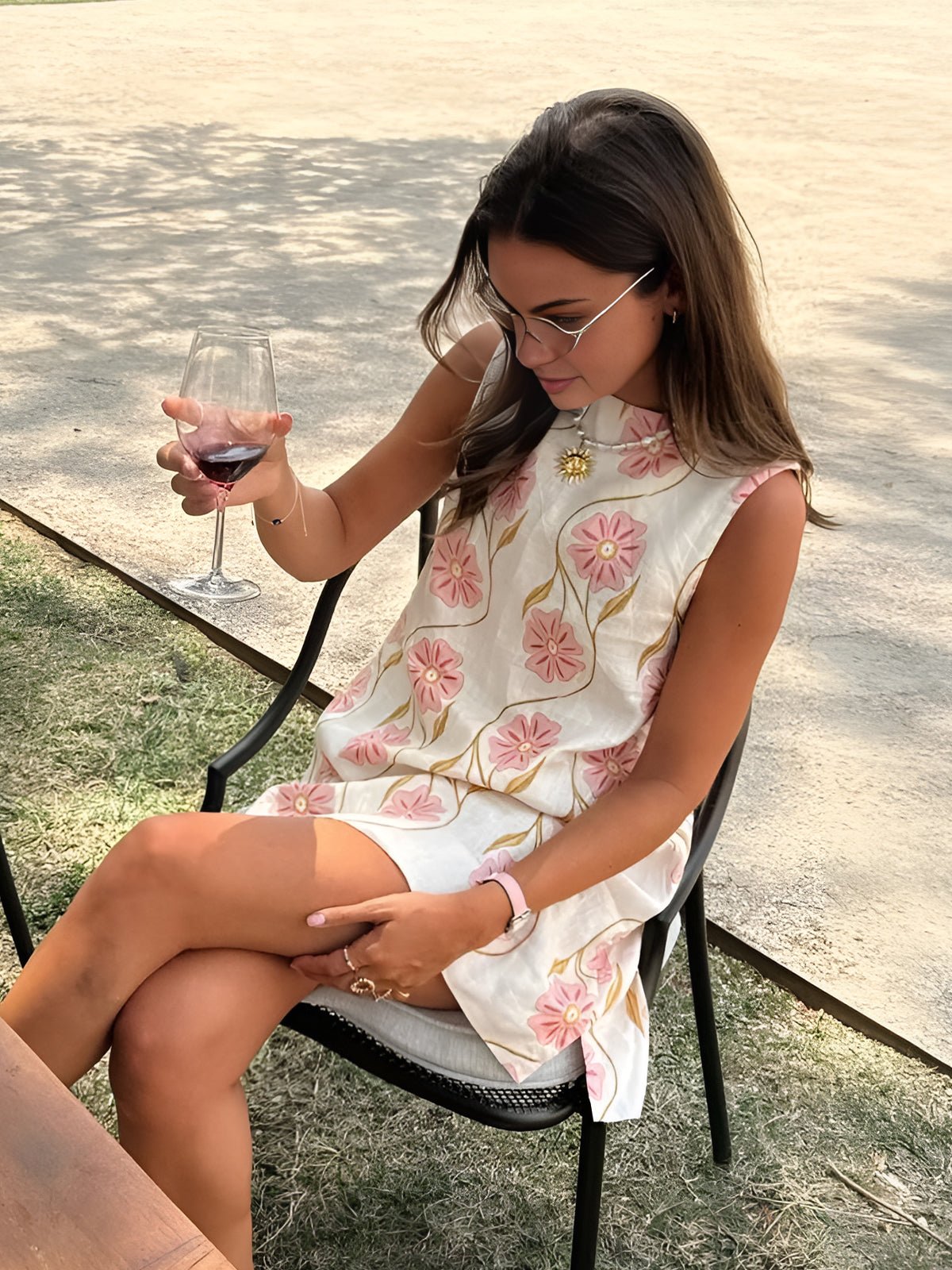 Woman in a floral dress holding a glass of red wine outdoors.