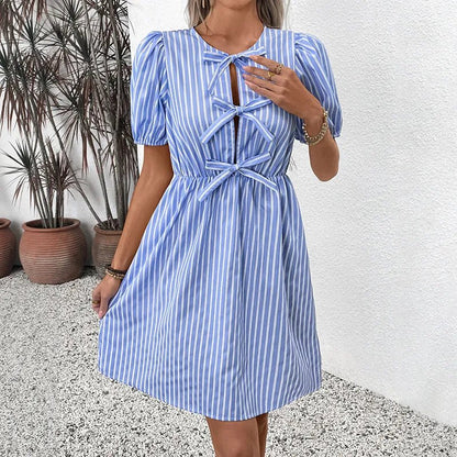 Woman wearing a blue and white striped dress with puffed sleeves against a white wall.
