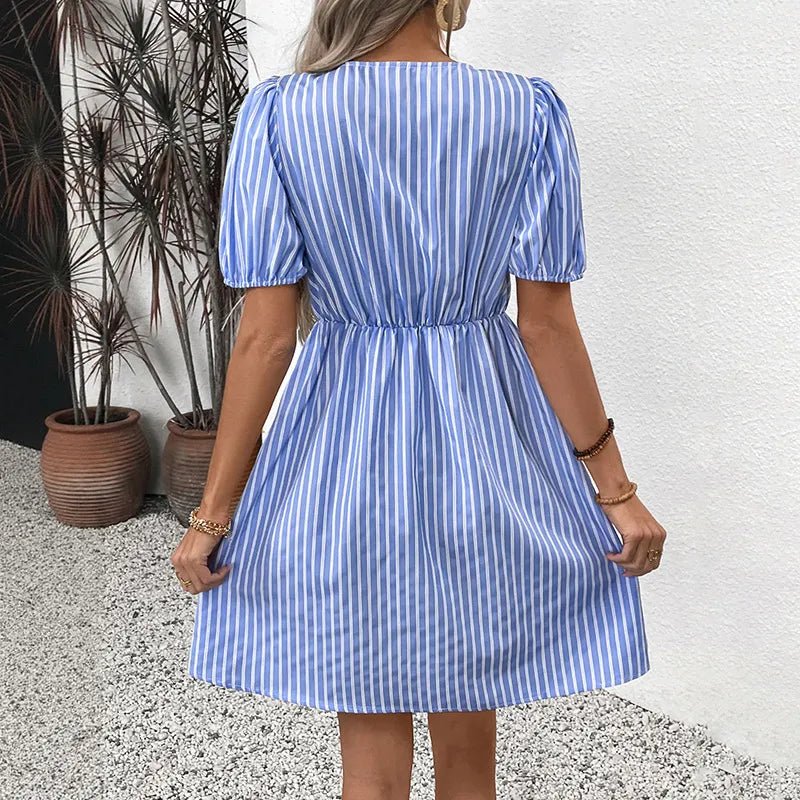 Woman wearing a blue and white striped dress against a white wall with plants.