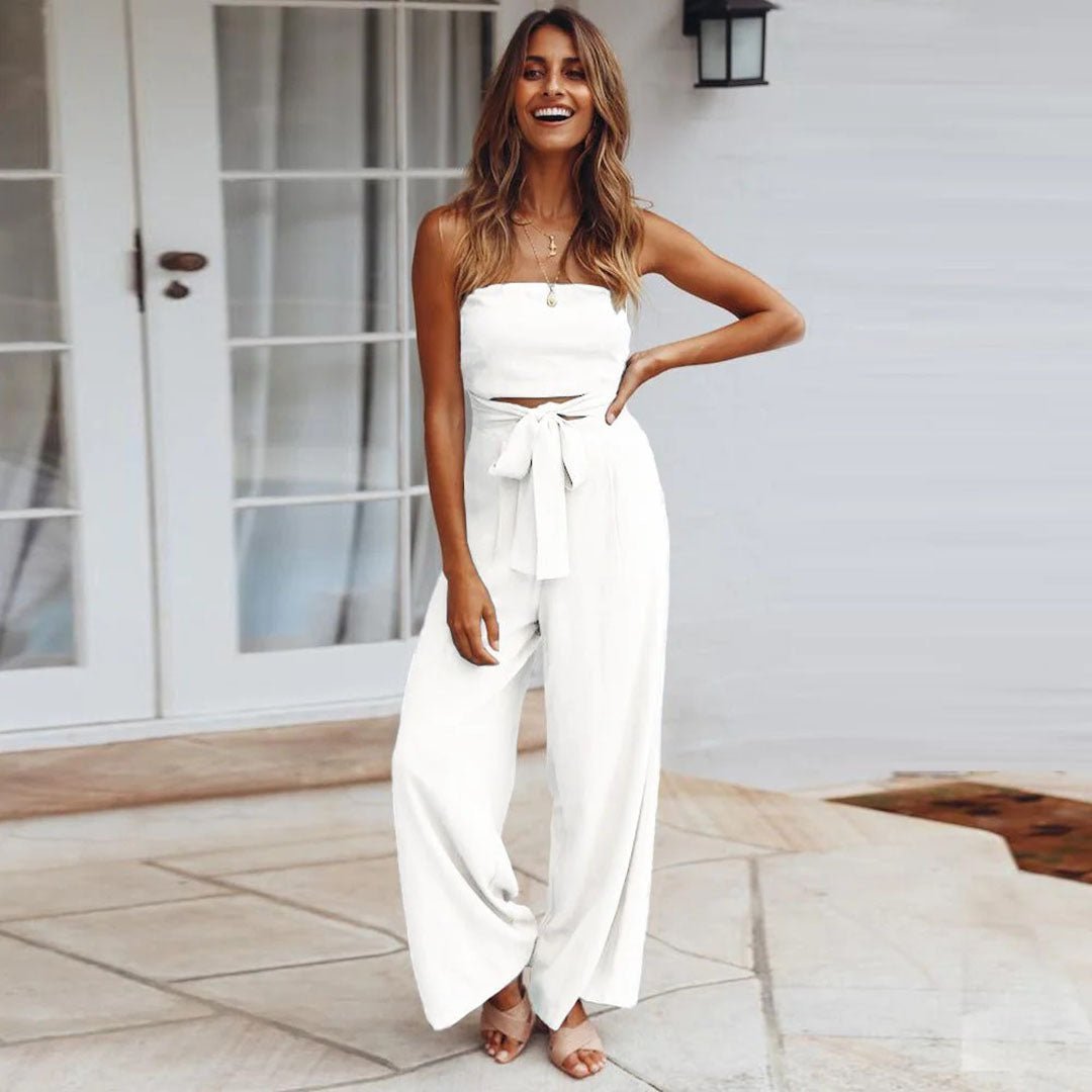 Woman wearing a white strapless top and wide-leg pants standing on a patio.