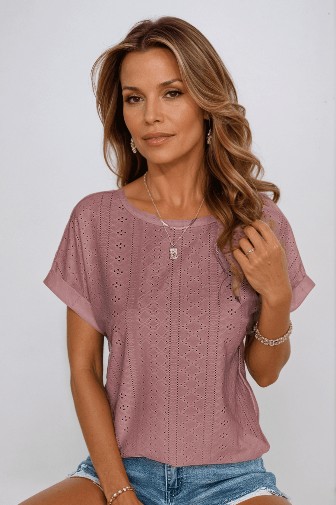 Woman wearing a pink lace top and denim shorts against a plain background